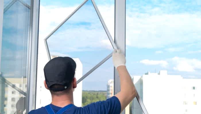 a worker in a blue uniform, rear view, installs a mosquito net in a plastic window frame, against the sky